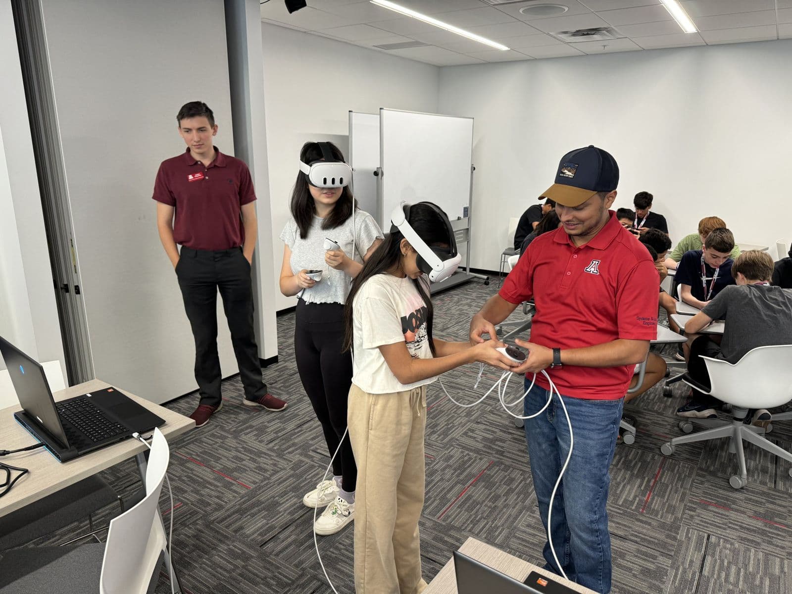 Sujan Ghimire guiding a student using a virtual reality headset and controllers while other students work in the background.