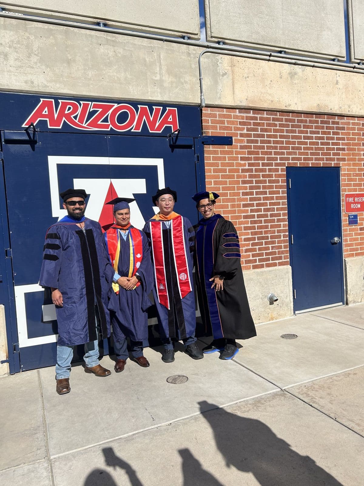 Sujan Ghimire with three others in graduation and doctoral regalia in front of the Arizona block-A logo.